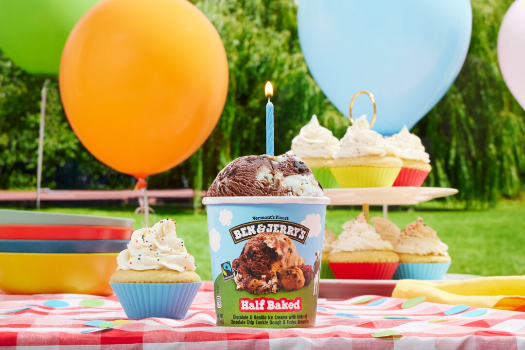 Ben & Jerry's ice cream pints on a picnic table with a balloon in a park.